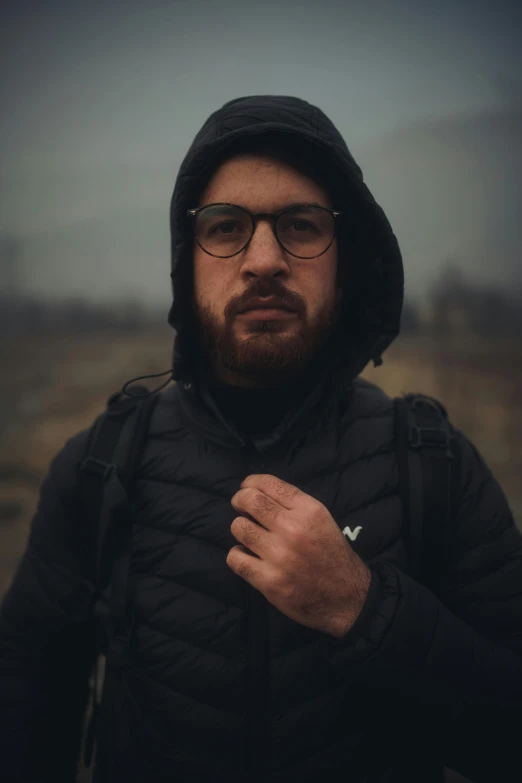 a bearded man in a jacket and hood is standing on the hill