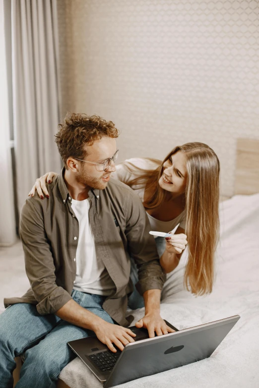 the man and woman are sitting on a bed with the laptop