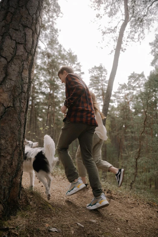 a man standing next to a white and black dog on top of a forest