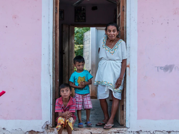 three children waiting outside a doorway with a woman