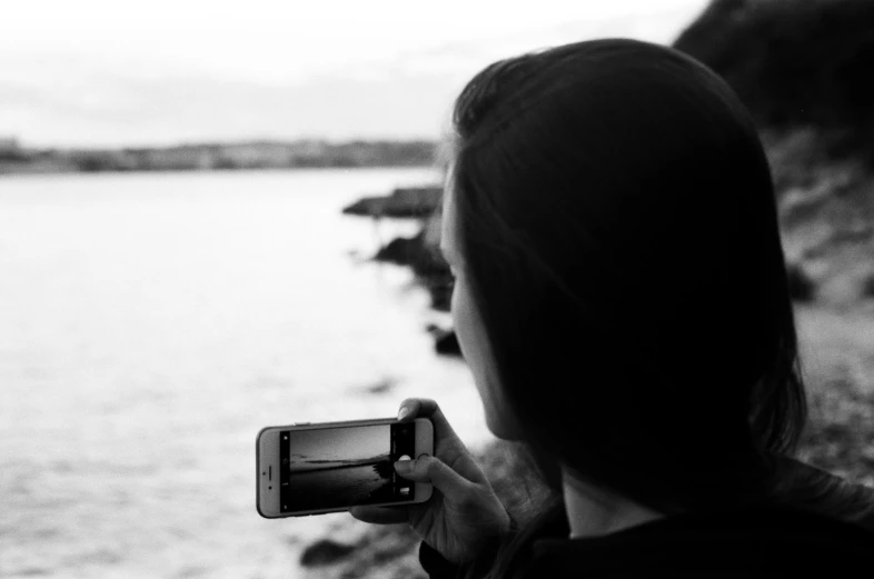 woman holding cellphone in front of body of water