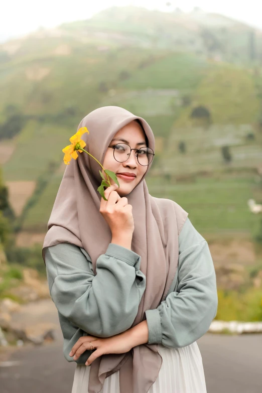 a woman in glasses wearing a hijab holding a flower