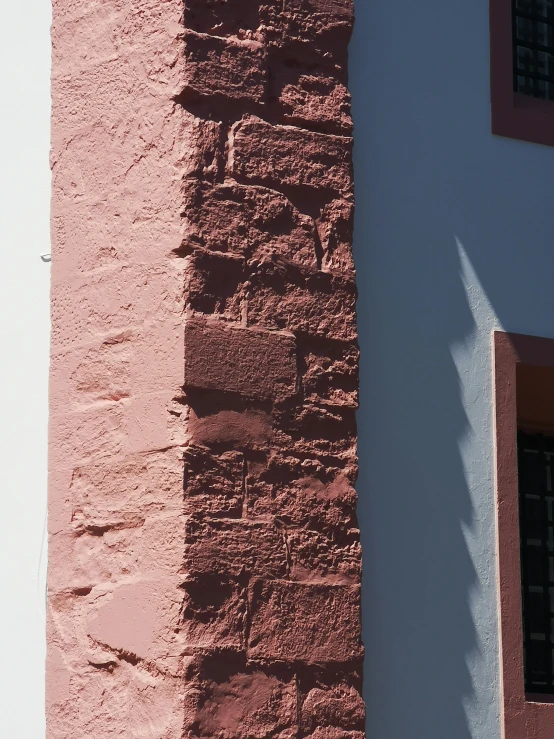 a red and white wall with windows under the shadow of a pigeon