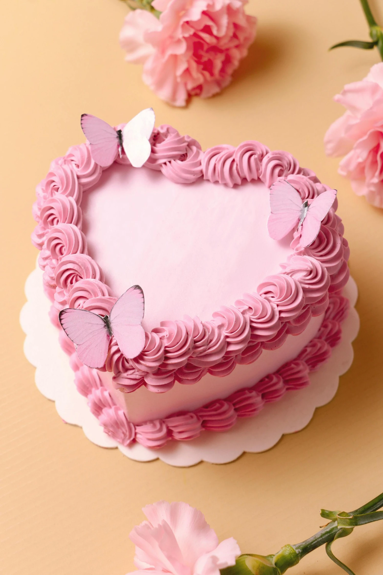 a pink heart shaped cake sits on a table with flowers