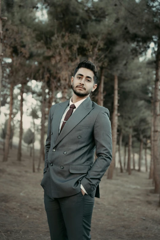 a man in a suit stands in a wooded area