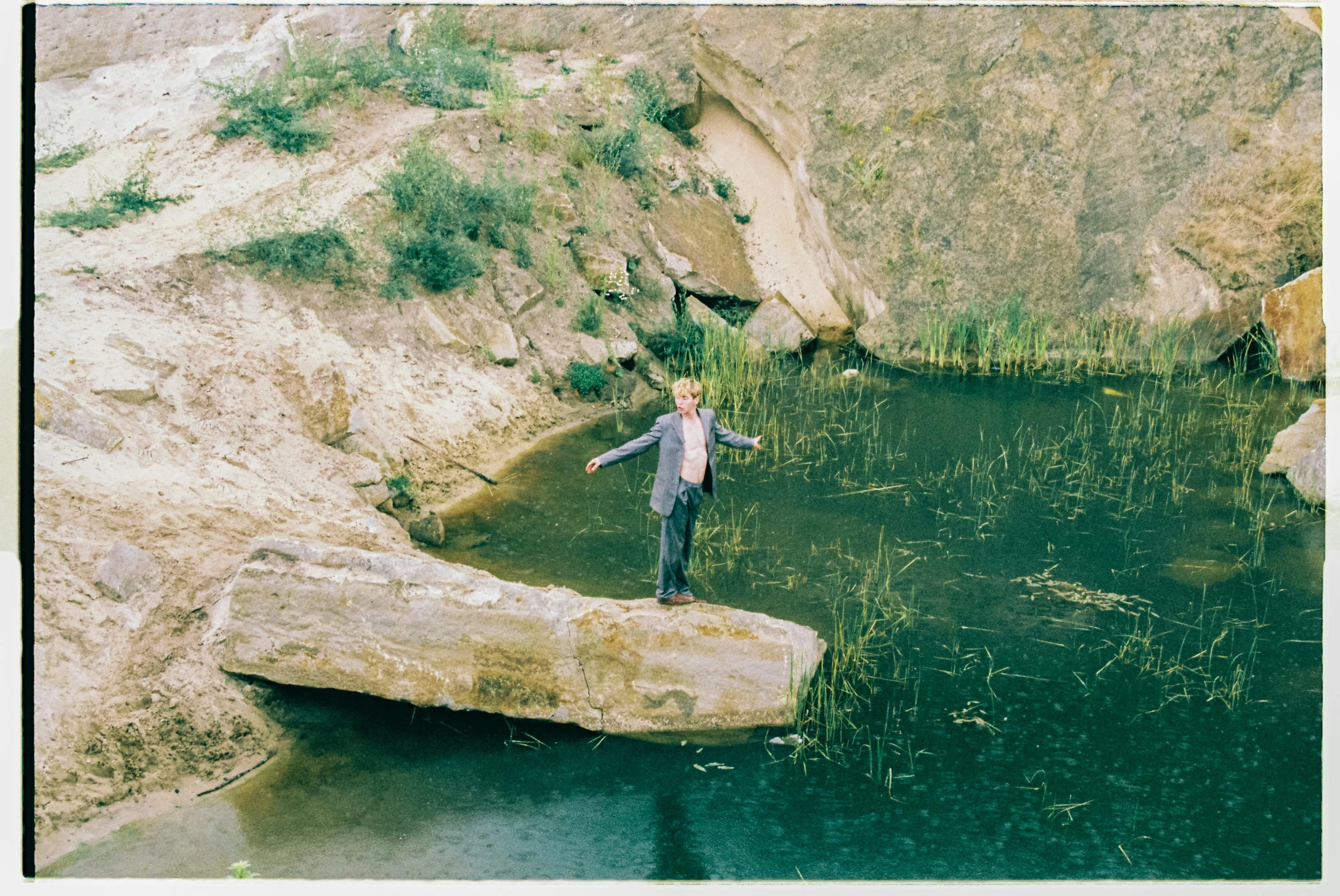 a boy standing in the middle of a stream next to a mountain