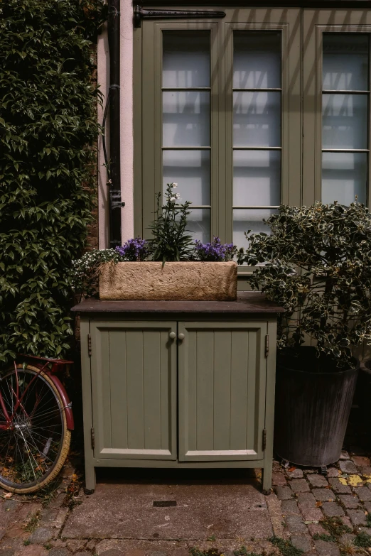 there is a green cabinet that has flowers and a bike in the background