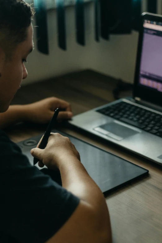 a person writing on paper next to a laptop