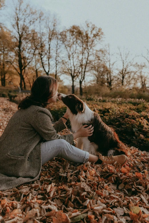 a lady in a coat kissing a dog while laying on the ground