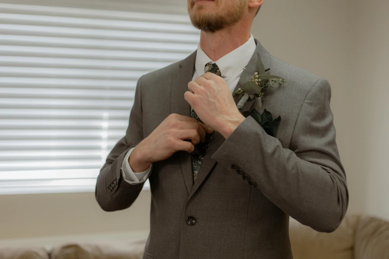 the man is adjusting his tie of his gray suit