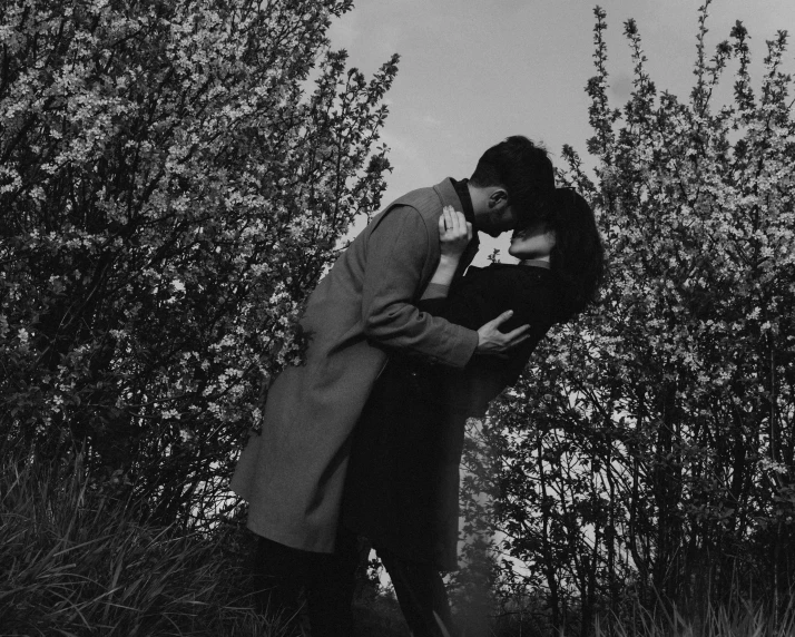 a woman kissing a man in front of bushes