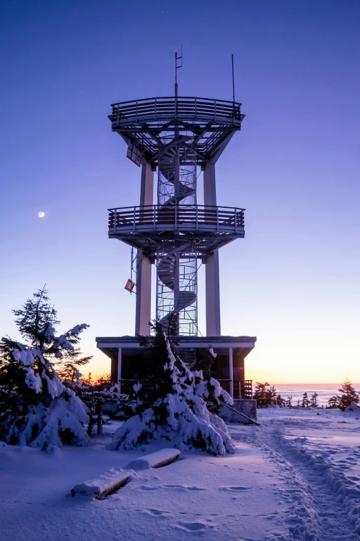 a very tall tower next to a few trees covered in snow