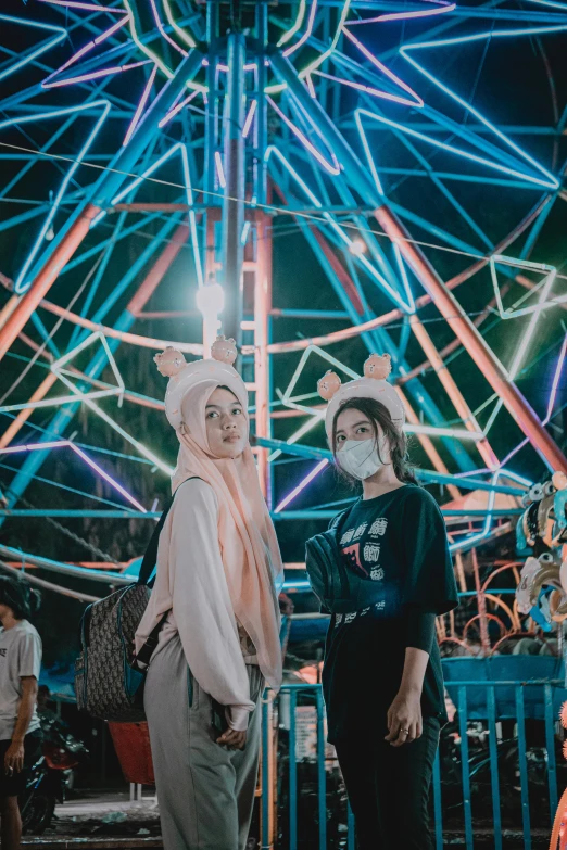 two women with masks on standing in front of a carnival ride