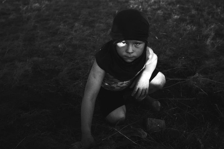 a woman in black with dark clothing crouching on grass