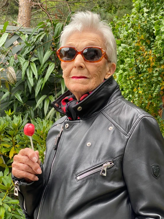 an old woman in black leather jacket holding flowers