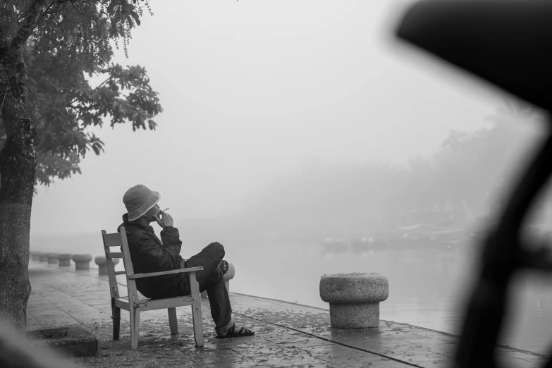 man sitting alone on bench talking on cellphone in heavy fog