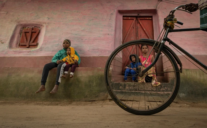 a woman, two girls and an old bike outside a building