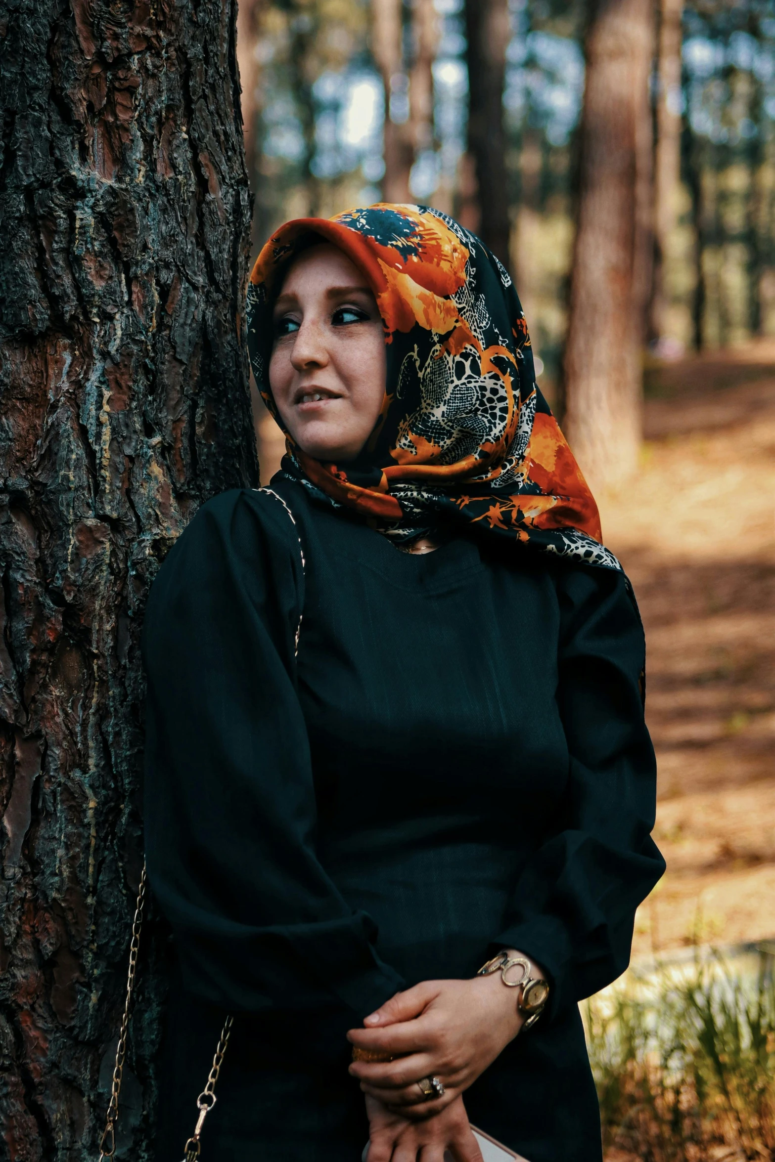 a woman with a red, orange and black hijab is leaning against a tree