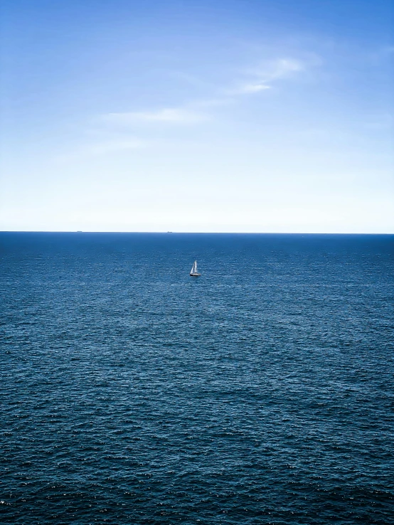 a lone boat in the middle of an ocean under a bright blue sky