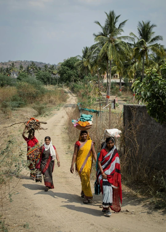 three women with colorful scarves walking down a dirt road