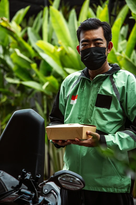 a man in a green outfit holding a cardboard box and wearing a face mask