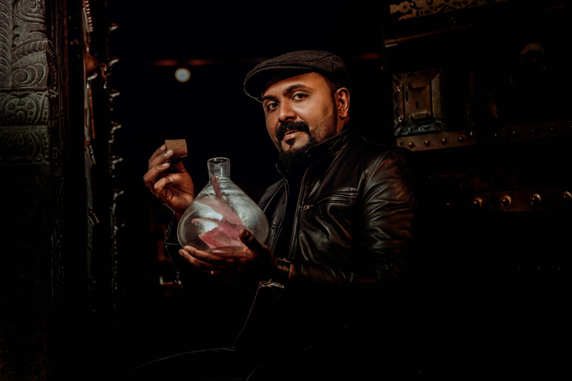 a man in black leather jacket holding up a glass bottle