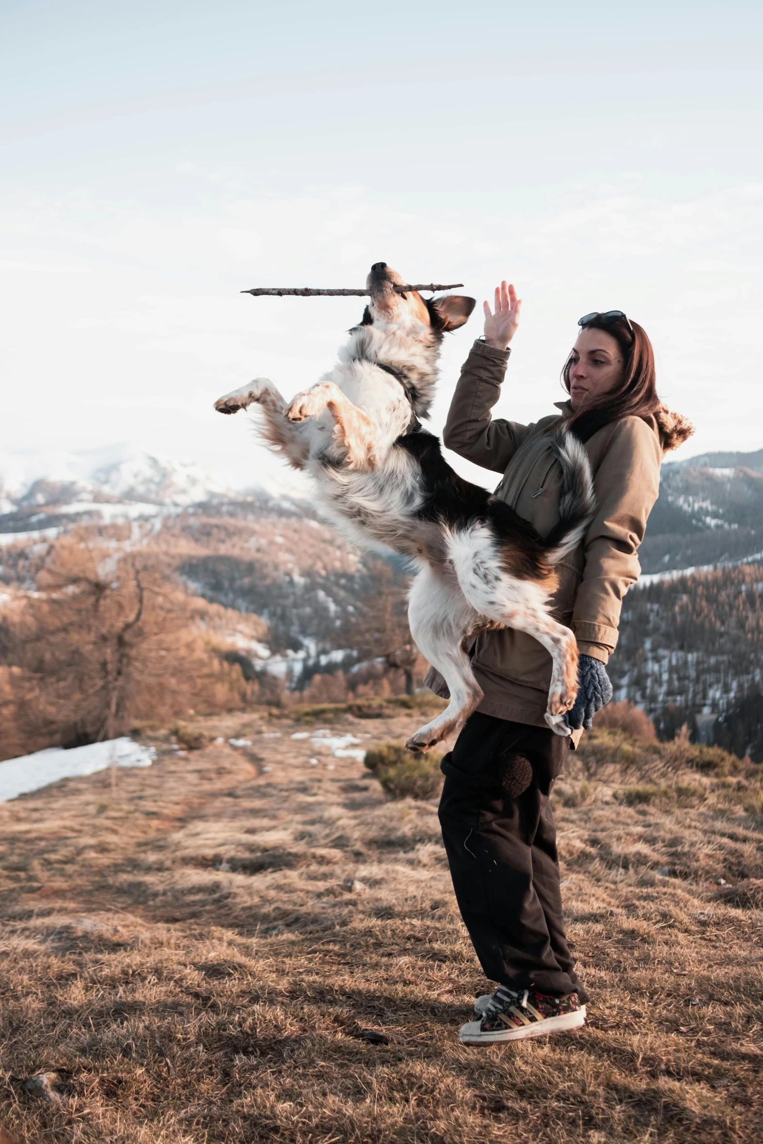 a woman holding her dog while standing on top of a mountain