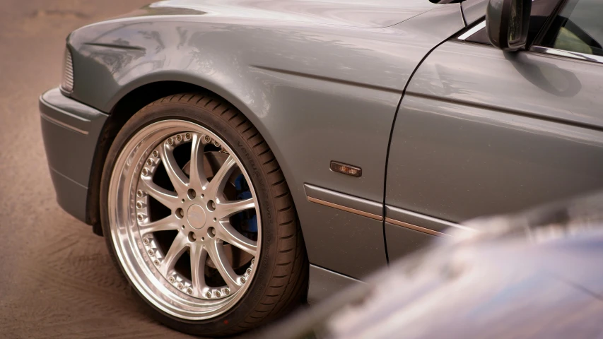 silver car with shiny wheels is parked near other cars