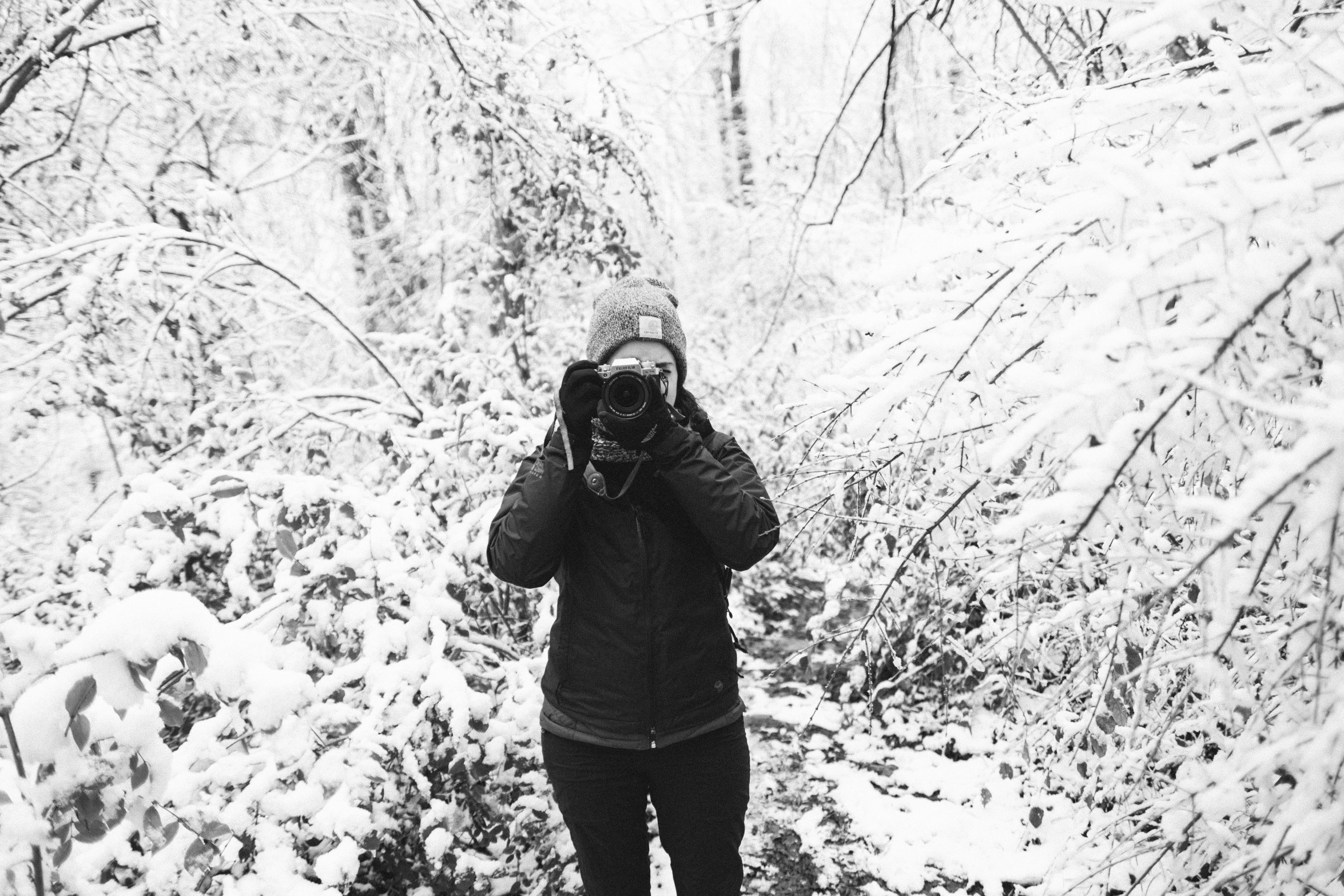 the person is taking a picture with his camera in a snowy forest