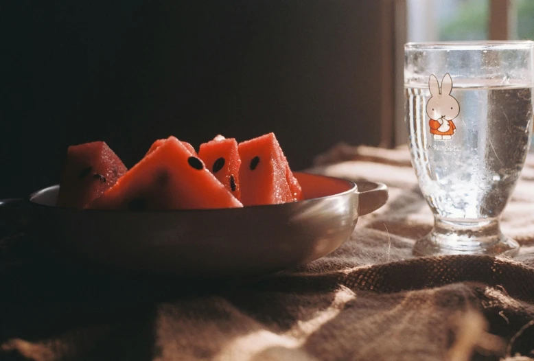 a plate and bowl with pieces of watermelon in front of a glass