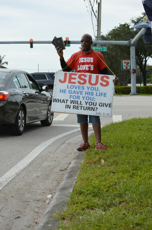 a man in a red shirt holding up a sign that says jesus