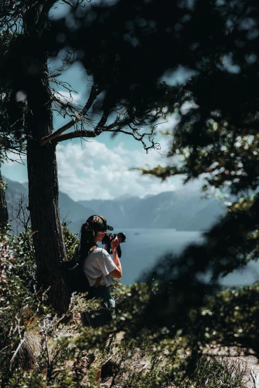 a person holding a camera and a lens standing near trees