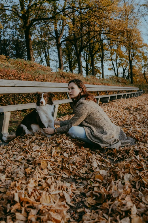 a woman with her dog is sitting in the leaves