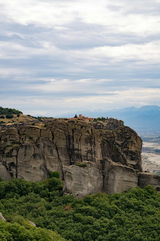 a tall rock cliff with grass and a lot of trees