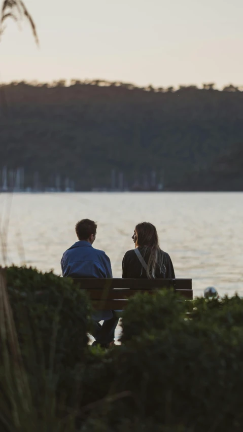 two people sitting on a bench next to a body of water