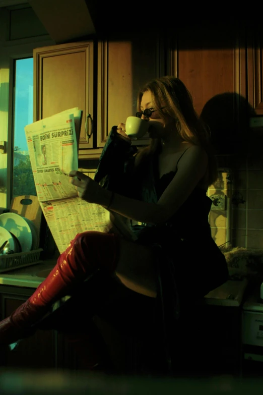 the woman is drinking from a cup, reading the newspaper