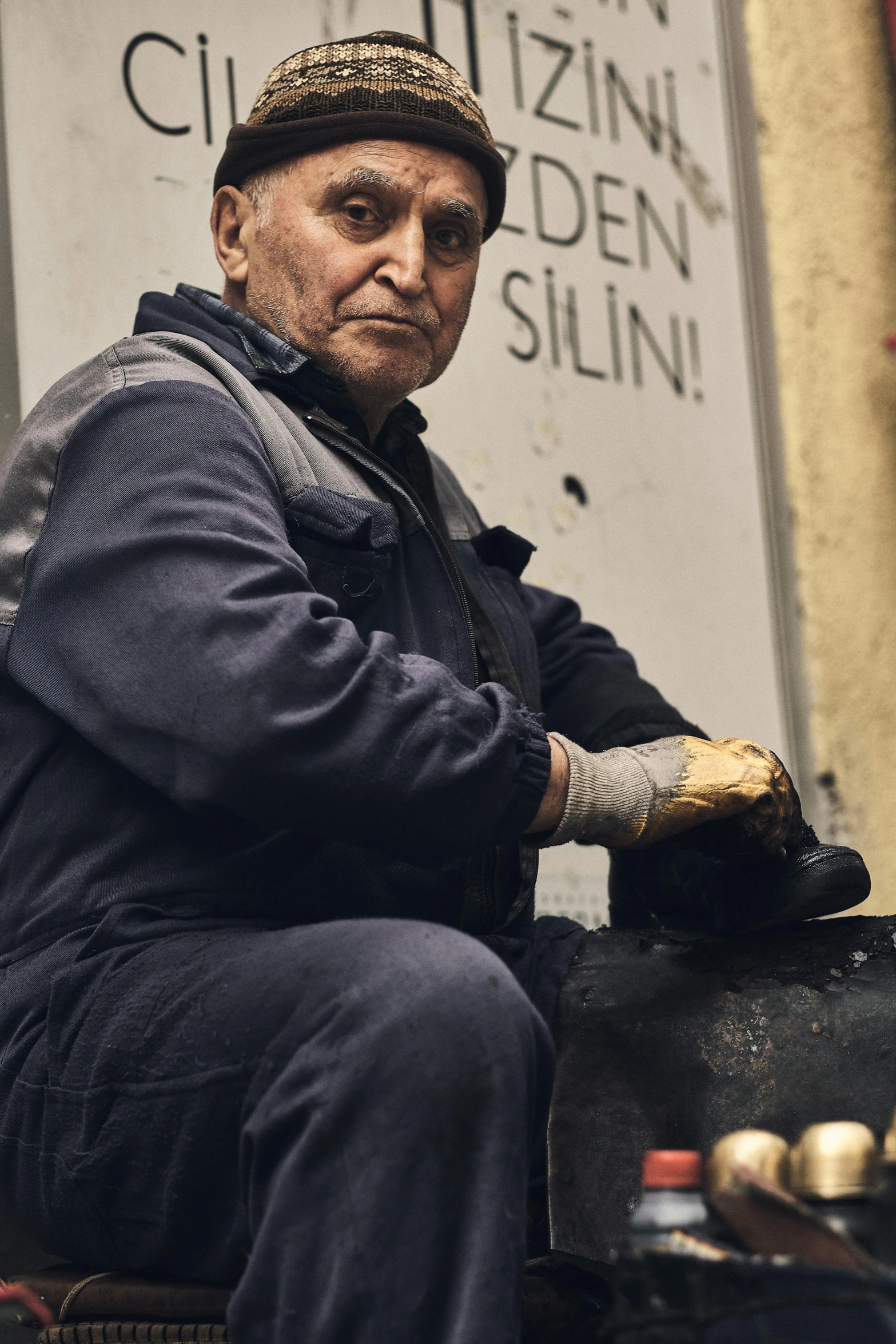 an elderly man with a baseball cap sits outside