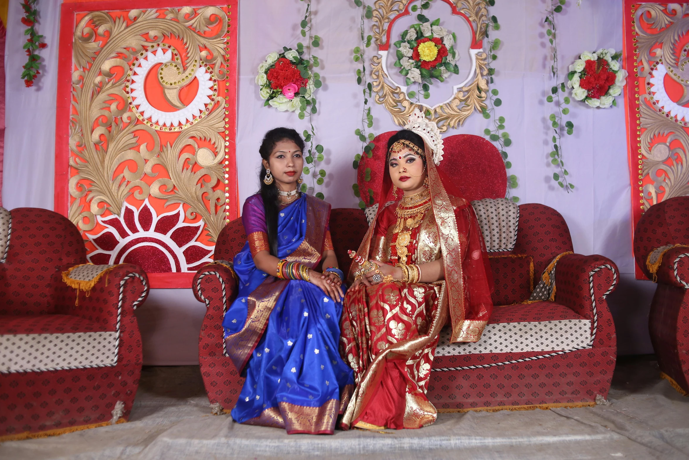 two women sitting on chairs wearing matching sari