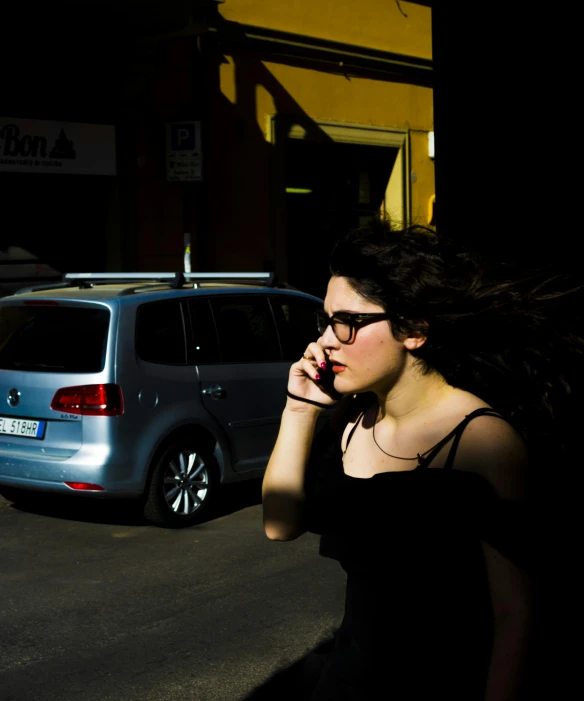 a lady in glasses and a black dress talks on her phone