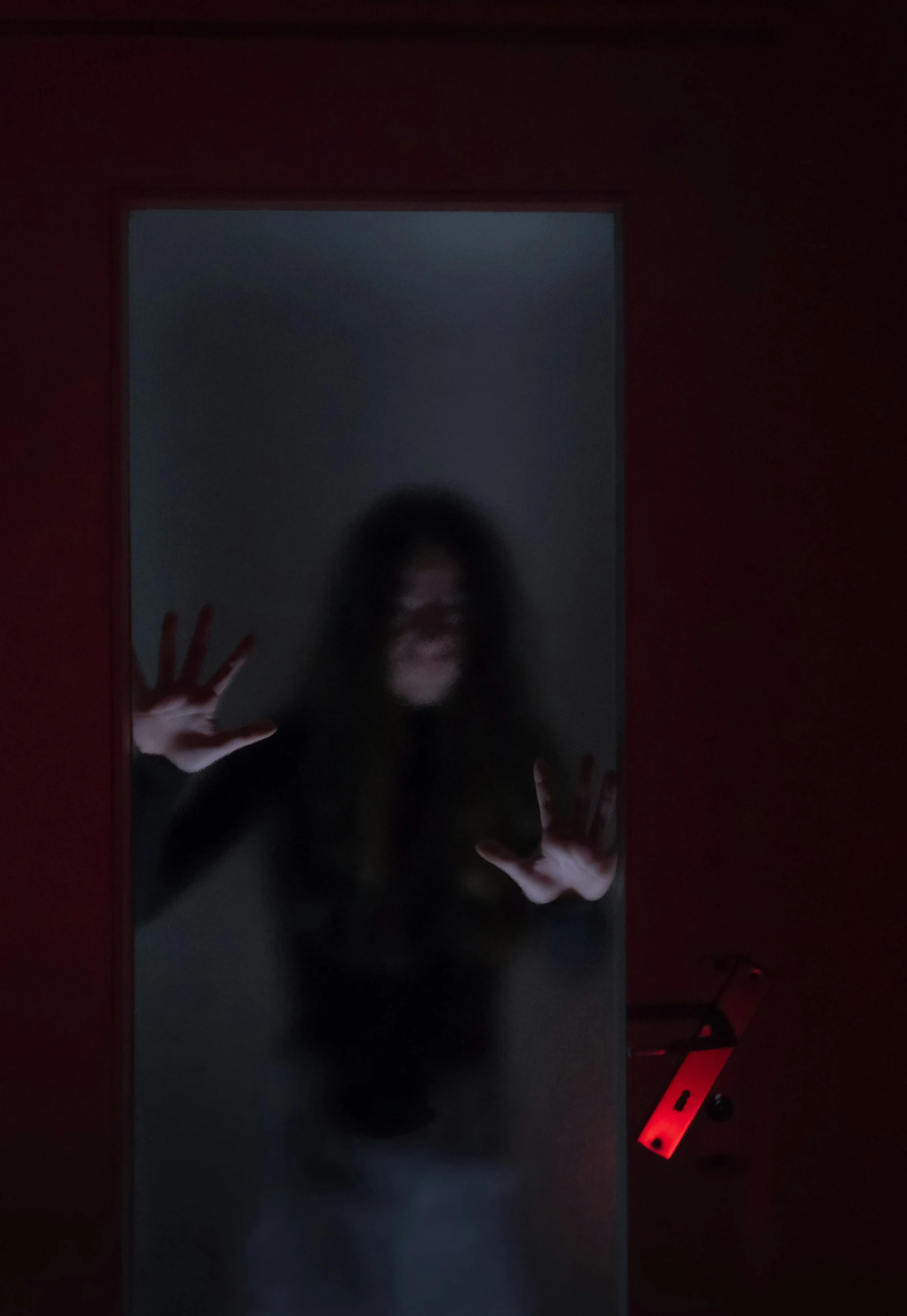 a dark room with red walls and a creepy woman standing in the doorway, holding out her hands