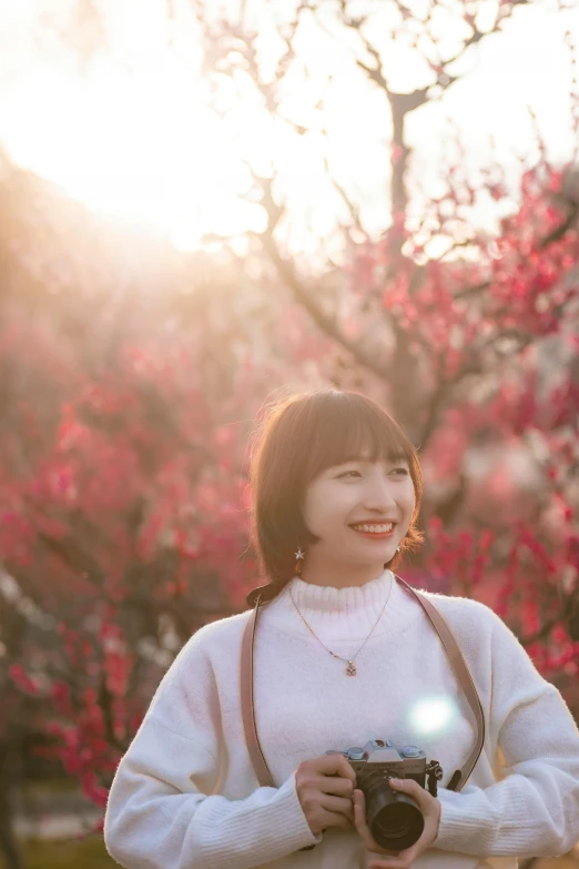 a woman wearing white holds a camera and smiling