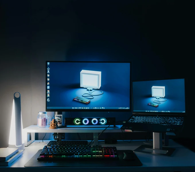 a computer and laptop on a desk with their lights turned on