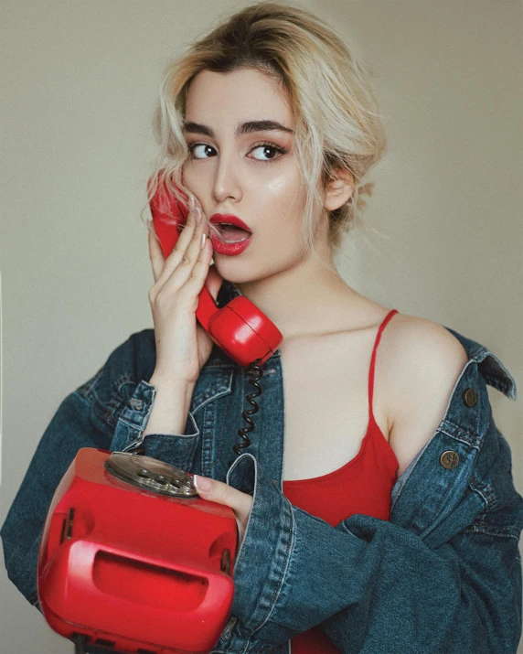 girl with blue jean jacket holding red cell phone in hands