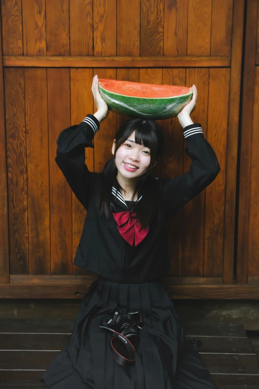 a girl sitting on the ground holding up a watermelon