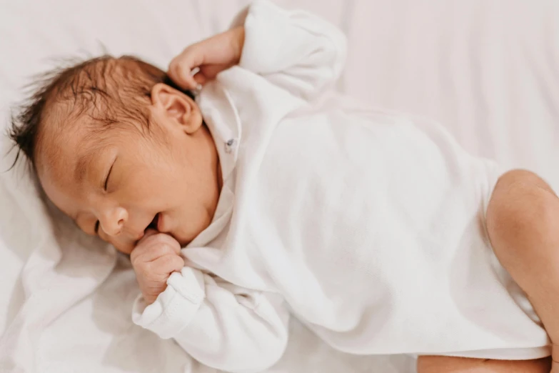 a baby sleeping in white sheets with a tiny finger