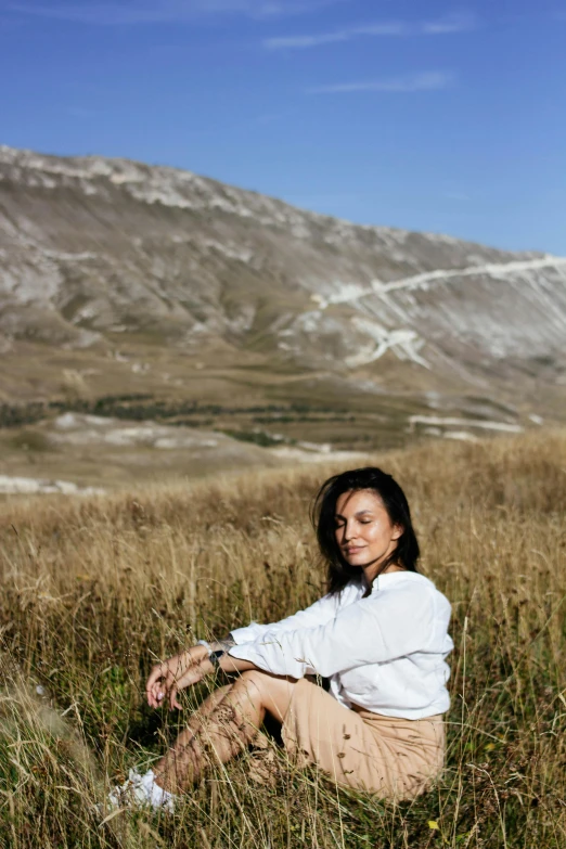 a woman sitting in a field with a snowy mountain in the background