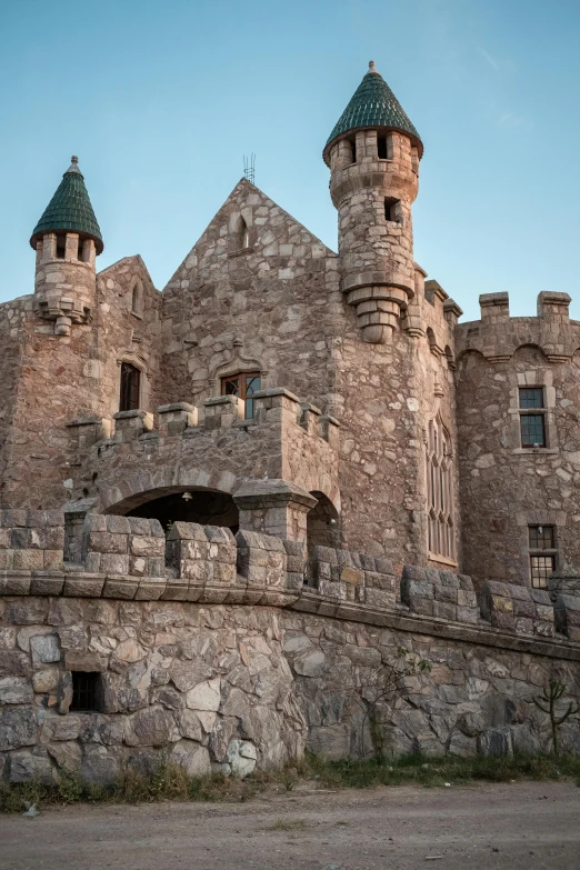 a castle like structure with three turrets sits on a hillside