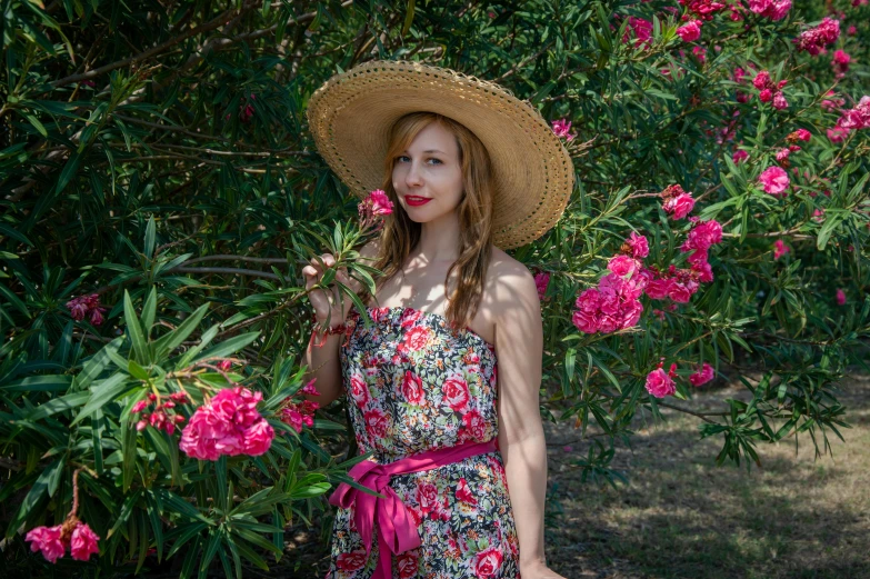 a woman in a dress and hat poses among pink flowers