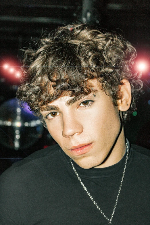 young man with curly hair and dark clothing posing