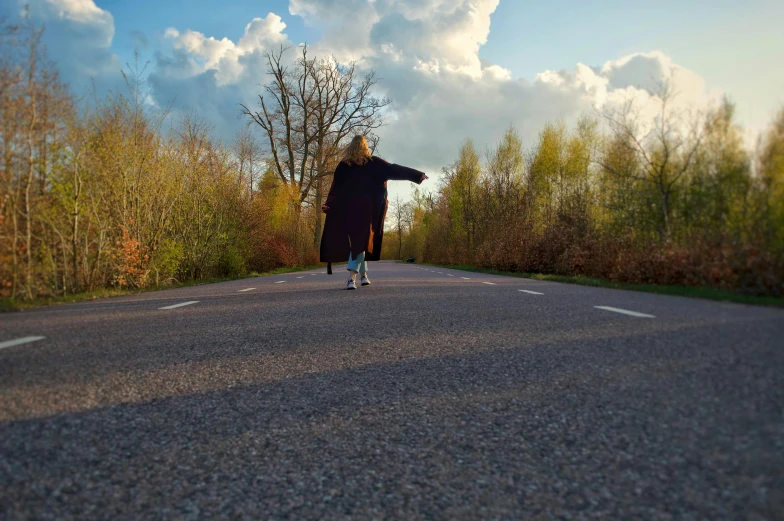 person on skateboard standing by roadway and trees